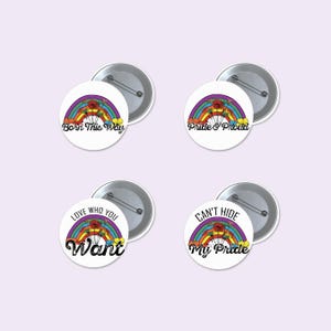 May include: Four circular pin-back buttons featuring a rainbow graphic with flowers and text. The buttons display the phrases Born This Way, Pride & Proud, Love Who You Want, and Can't Hide My Pride in black lettering against a white background.