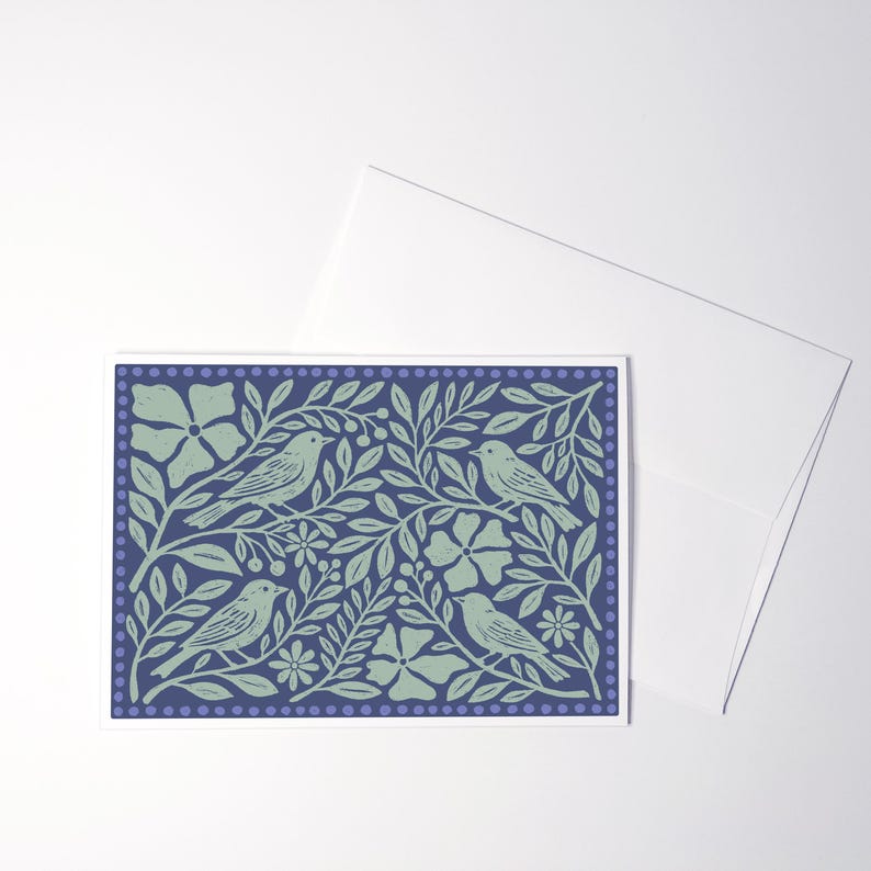 Puede incluir: Una tarjeta de felicitaci&oacute;n rectangular con fondo azul oscuro y un patr&oacute;n de impresi&oacute;n en bloque verde claro de cuatro p&aacute;jaros posados entre hojas, flores y bayas estilizadas, enmarcado por un borde de puntos peque&ntilde;os, junto a un sobre blanco.
