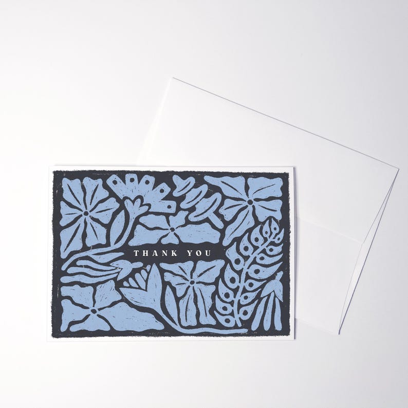 K&ouml;nnte beinhalten: Eine rechteckige Gru&szlig;karte mit dunkelblauem Hintergrund, einem hellblauen Blumenmuster und dem Text THANK YOU, der in einem dunkelblauen horizontalen Balken zentriert ist. Ein schlichter wei&szlig;er Umschlag liegt hinter der Gru&szlig;karte.