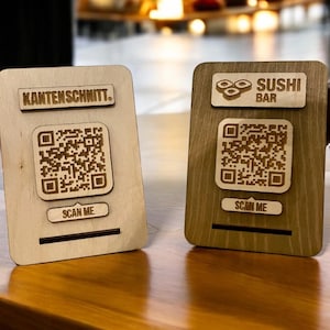 Könnte beinhalten: Zwei Holzschilder mit QR-Codes und Text. Das Schild links sagt "Kantenschnitt". Das Schild rechts sagt "Sushi Bar". Beide Schilder haben den Text "Scan Me" unter dem QR-Code.