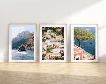 May include: Three framed photographs of the Amalfi Coast in Italy. The first photo shows a rocky cliffside with a boat in the water. The second photo shows a colorful village built into the hillside. The third photo shows a large tree growing on a cliff overlooking the sea.