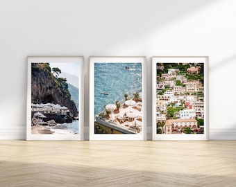 May include: Three framed photographs of an Italian coastal town. The first photo shows a rocky cliffside with a beach below. The second photo shows a rooftop terrace with white umbrellas and chairs. The third photo shows a hillside with colorful buildings.