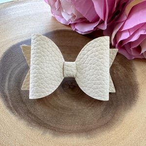 May include: A cream-colored faux leather bow with a textured surface.