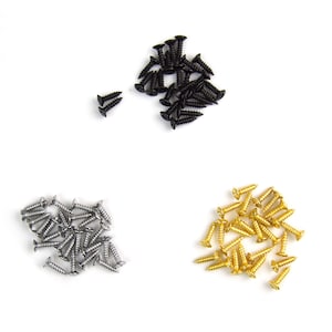 May include: Three piles of screws in different colours: black, silver, and gold. The screws are small and have a flat head.