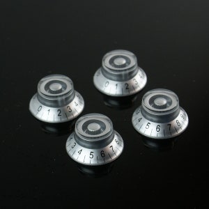 Pode incluir: Quatro botões de guitarra prateados com números pretos. Os botões são numerados de 0 a 4, de 0 a 4, de 5 a 9 e de 3 a 8.