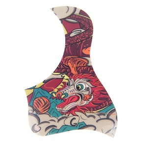 Puede incluir: Una púa de guitarra colorida con un diseño de dragón. El dragón es rojo, amarillo y verde con un fondo blanco. La púa tiene forma de lágrima.