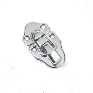 May include: A chrome-plated metal latch with a curved design and a spring-loaded mechanism. The latch has four holes for mounting.