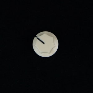 May include: White plastic knob with a black line on the top. The knob has six sides.