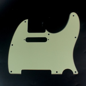 Może przedstawiać: Jasnozielony pickguard do gitary z czarnym wycięciem na przetwornik i wieloma otworami na śruby.