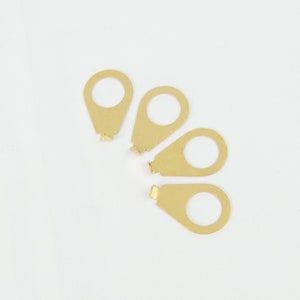 May include: Four gold-colored metal guitar strap buttons. The buttons are shaped like a teardrop with a round hole in the center.