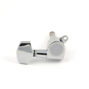 May include: A chrome-plated guitar tuning peg featuring a metallic finish, a trapezoidal tuning key, a cylindrical post, and a mounting flange with a small screw hole. The mechanism is designed for string tension adjustment on a musical instrument.