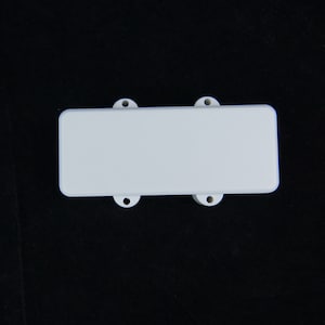 May include: White plastic cover for a guitar pickup. It has four screw holes.