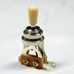May include: A chrome-plated guitar toggle switch with a cream-coloured knob. The switch has three terminals and is designed for use in electric guitars.