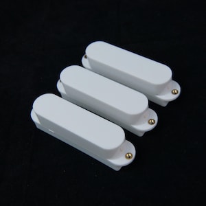 May include: Three white guitar pickups with gold screws. The pickups are arranged in a row, with the top pickup slightly offset to the right.