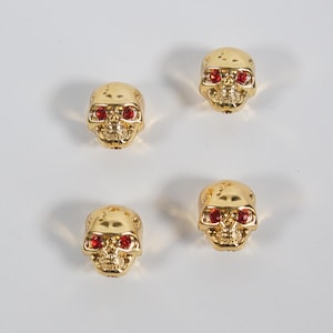 Op de afbeelding: Vier gouden, schedelvormige gitaar stemknoppen met rode strass steentjes als ogen.