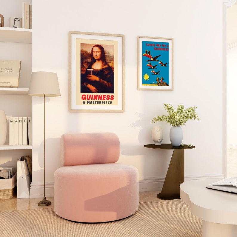 May include: A pink round armchair with a cylindrical back, a white lamp, a small round side table with a vase of white flowers, and two framed posters on a white wall. One poster features a painting of the Mona Lisa with the text "GUINNESS A MASTERPIECE" and the other poster features a blue background with the text "Lovely day for a GUINNESS" and a group of toucans flying.