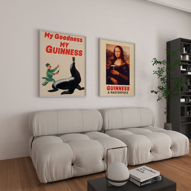 May include: Two framed posters with a white background. The poster on the left features a cartoon illustration of a man in a green shirt and a seal holding a glass of Guinness beer. The text on the poster reads "My Goodness My Guinness". The poster on the right features a painting of the Mona Lisa holding a glass of Guinness beer. The text on the poster reads "Guinness A Masterpiece".