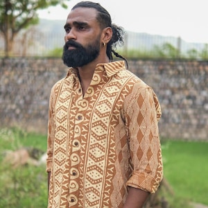 Puede incluir: Camisa abotonada con estampado geométrico en tonos marrón y crema. La camisa tiene mangas largas y cuello. La tela parece ligera, adecuada para climas cálidos. La camisa está desabrochada en la parte superior. Patrón repetitivo.