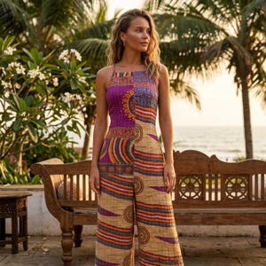 Op de afbeelding: Een kleurrijke jumpsuit met een halterhalslijn. De top is paars met een cirkelvormig ontwerp, terwijl de broek een beige achtergrond heeft met oranje, paarse en blauwe strepen. De jumpsuit is gemaakt van een patroonstof.