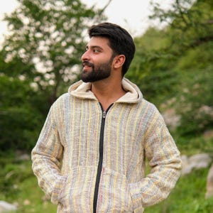 May include: A hooded jacket with a vertical striped pattern in yellow, blue, and red. The jacket has a black zip and a cream-coloured hood lining. The person is wearing the jacket and looking to the side.