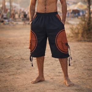May include: Navy blue cargo shorts with rust-colored circular accents and pockets. The shorts have black trim and drawstrings at the bottom. The shorts are knee-length and appear to be made of a lightweight fabric.