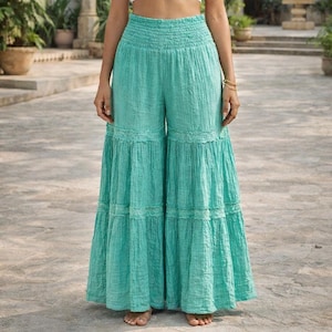 May include: Turquoise palazzo pants with a smocked waistband and tiered, ruffled hems. The wide-leg pants feature delicate lace trim and a flowing, lightweight fabric, perfect for warm weather. The pants are a solid color and have a relaxed fit.