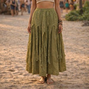 Puede incluir: Falda larga verde oliva con una superposición de encaje y detalles de flecos. La falda tiene una cintura alta y una silueta fluida, perfecta para un look bohemio o festivalero. Hecha de una tela ligera, ideal para el clima cálido.
