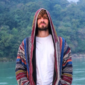 May include: A colourful, patterned hooded jacket. The jacket has a mix of red, blue, orange, and yellow stripes and geometric patterns. The person is wearing a white t-shirt under the jacket.
