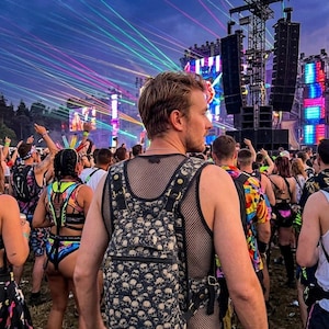 May include: A black mesh tank top worn with a black backpack featuring a repeating white skull pattern. The backpack has adjustable straps with gold-toned metal hardware, a zippered front pocket, and a structured design worn over the shoulders.