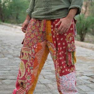 May include: Patchwork cargo pants featuring a vibrant mix of red, yellow, and pink fabric panels with intricate floral and geometric patterns. These loose-fitting trousers include side cargo pockets with flaps and a visible running stitch detail.