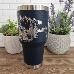 May include: A navy blue stainless steel tumbler with a laser-etched design of a semi-truck driving through a mountain landscape with trees and a lake. The design is in silver.