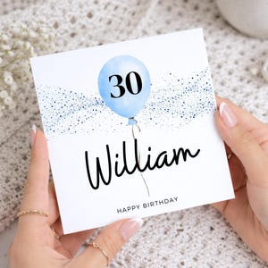 Può includere: Un biglietto d'auguri di compleanno quadrato e bianco con un palloncino azzurro su cui è stampato il numero 30 in nero. Il design include accenti glitter blu, il nome William in corsivo nero e il testo HAPPY BIRTHDAY in lettere maiuscole.