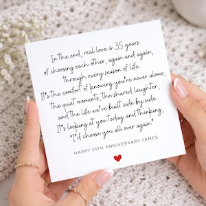 May include: A square white card featuring black cursive text that reads: In the end, real love is 35 years of choosing each other, again and again. Through every season of life. It's the comfort of knowing you're never alone, the quiet moments, the shared laughter, and the life we've built side by side. It's looking at you today and thinking, I'd choose you all over again! HAPPY 35TH ANNIVERSARY JAMES, with a small red heart icon below.
