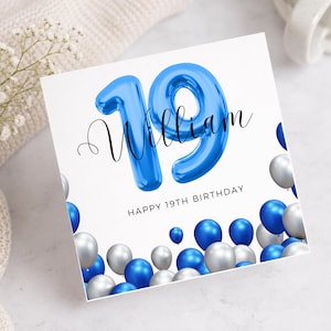 May include: A white birthday card with the name "William" in cursive and the number "19" in blue balloon style. The card reads "HAPPY 19TH BIRTHDAY" and is decorated with blue and silver balloons.