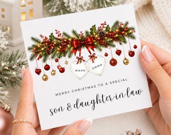 May include: A square white Christmas greeting card featuring a festive illustration of pine branches, red berries, and a large red bow. Two heart-shaped ornaments are personalised with the names Mark and Emma. Text reads: MERRY CHRISTMAS TO A SPECIAL son & daughter-in-law.