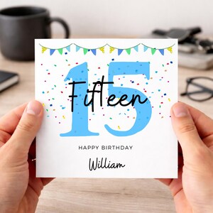 Peut inclure: Carte d'anniversaire avec le chiffre "15" en bleu clair et le mot "Fifteen" en écriture noire. La carte dit également "Happy Birthday William" avec des confettis et une bannière.
