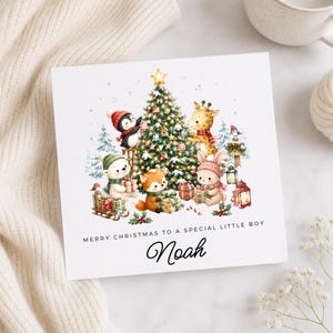 May include: A square Christmas greeting card featuring a decorated pine tree surrounded by a penguin, polar bear, fox, giraffe, and rabbit with gifts. The text reads MERRY CHRISTMAS TO A SPECIAL LITTLE BOY and the name Noah in black script.
