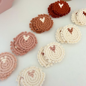 May include: Set of six handmade macrame coasters in three colors: cream, light pink, and terracotta. Each coaster features a white triangle design in the center.