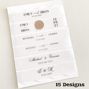 May include: A white card featuring transparent strips with names and dates printed in black. Names include "Emily and Brian," "Michael and Gemma," and "E & M." A small, circular, tan sticker is present. The text "15 Designs" is at the bottom of the card.
