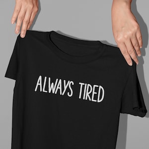 K&ouml;nnte beinhalten: Schwarzes T-Shirt mit wei&szlig;em Text, der "ALWAYS TIRED" lautet.