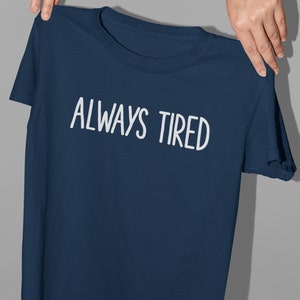 K&ouml;nnte beinhalten: Ein marineblaues T-Shirt mit wei&szlig;em Text, der "ALWAYS TIRED" lautet.