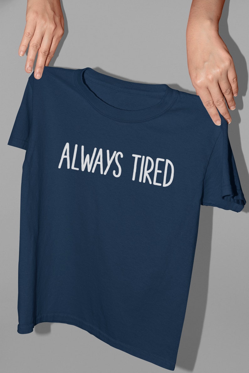 K&ouml;nnte beinhalten: Ein marineblaues T-Shirt mit wei&szlig;em Text, der "ALWAYS TIRED" lautet.