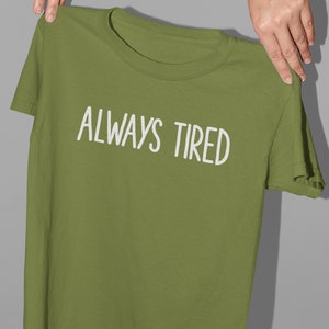 K&ouml;nnte beinhalten: Ein gr&uuml;nes T-Shirt mit dem Text "ALWAYS TIRED" in wei&szlig;en Buchstaben.