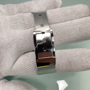 May include: A silver metal watch band with a buckle closure.
