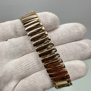 May include: A gold-tone watch band with a textured, ridged design. The band is made of metal and has a polished finish.