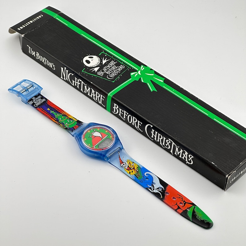 May include: A blue and green wristwatch with a Nightmare Before Christmas design. The watch face is blue and features a white Jack Skellington character. The watch band is blue and features a colorful design of Jack Skellington, Sally, and the Christmas tree. The watch comes in a black box with the words "Tim Burton's Nightmare Before Christmas" printed on it.
