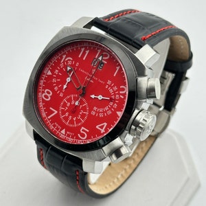 May include: A red chronograph wristwatch with a black leather band and silver accents. The watch face features the text "CHRISTIAN VAN SANT Aylion" and the numbers 1 through 12. The watch has a date window at the 12 o'clock position.