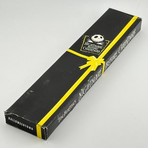 May include: A black box with yellow accents and the text "Tim Burton's Nightmare Before Christmas" and "Halloweentown". The box features a cartoon image of Jack Skellington, the main character from the movie.