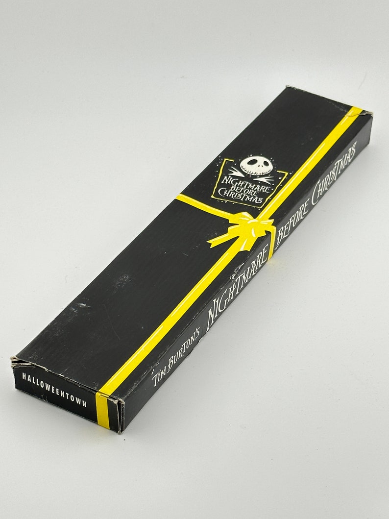 May include: A black box with yellow accents and the text "Tim Burton's Nightmare Before Christmas" and "Halloweentown". The box features a cartoon image of Jack Skellington, the main character from the movie.