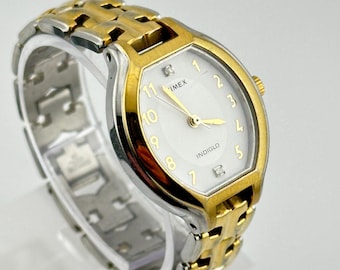 May include: A gold and silver-toned Timex Indiglo watch. The watch has a white face with gold hands and numerals. The watch band is a combination of gold and silver links.